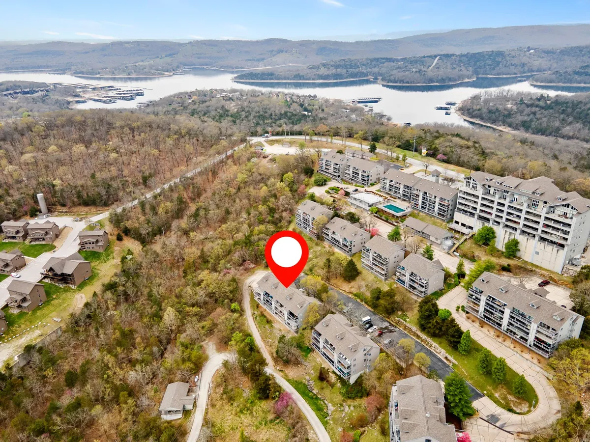 A sweeping view of the lake framed by forest, with residential buildings and winding roads visible. The tranquil water, lush greenery, and distant structures suggest a peaceful resort atmosphere and easy access to outdoor activities for all ages.