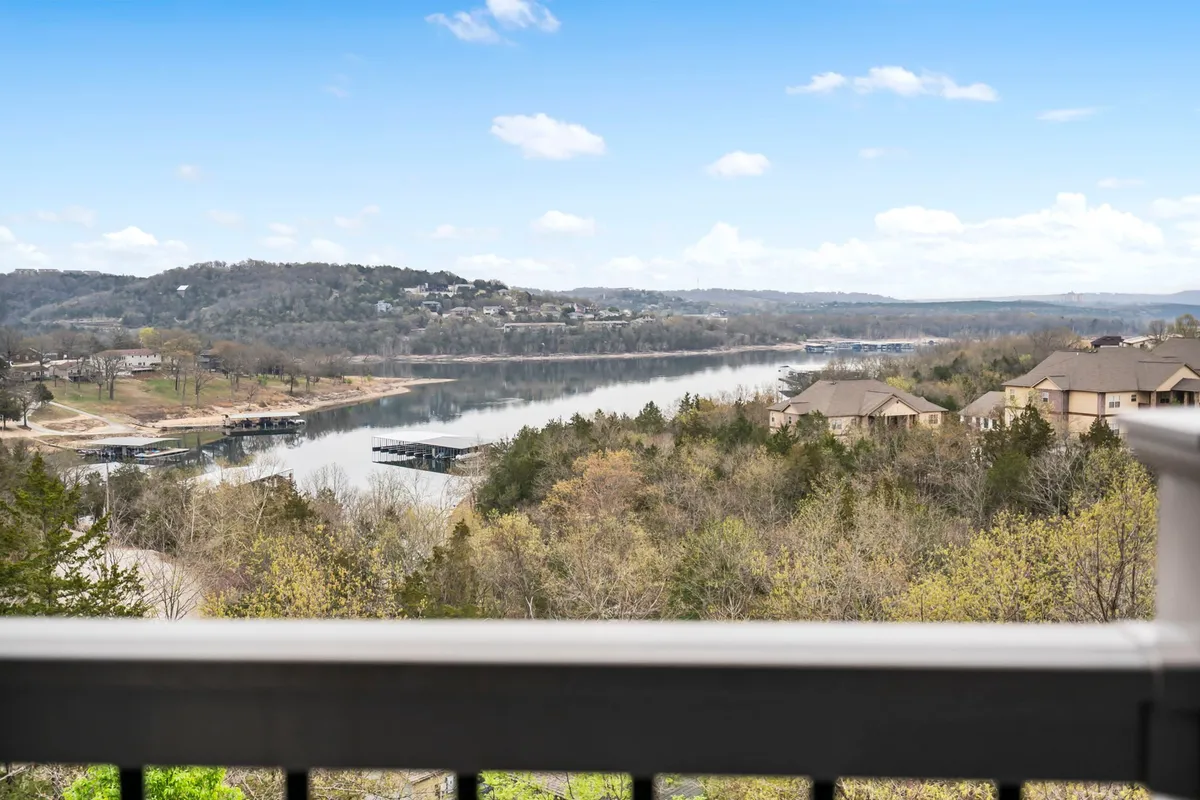 A sweeping view of Table Rock Lake with sparkling blue water, distant wooded hills framing the scene, and small marinas nestled along the shoreline. The ambiance is tranquil, with signs of boating and fishing activities, and the soft glow of sunset or early morning mist lending a serene atmosphere.