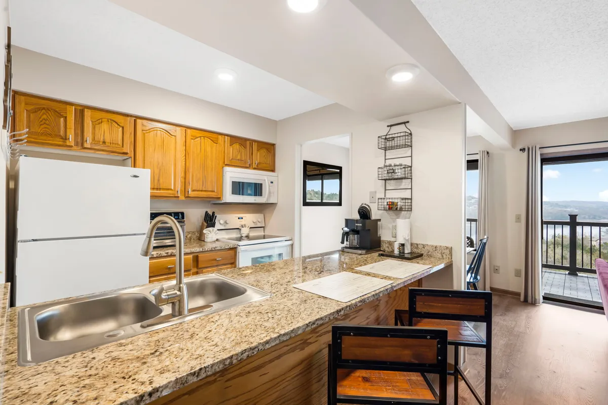 Here, a granite countertop pairs with wooden cabinets and stainless steel appliances, seamlessly connecting to a dining area set with chairs. The view between kitchen and dining zones emphasizes the open-plan design, ideal for family meals and group gatherings.