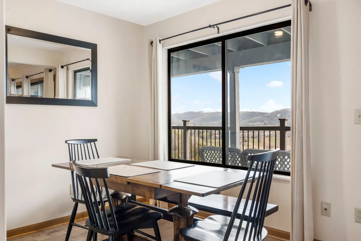 A light-filled dining table sits next to a window that offers a scenic view, with a decorative mirror reflecting the inviting space. The setup is perfect for family meals, intimate gatherings, or morning coffee, all in a comfortable, welcoming atmosphere.