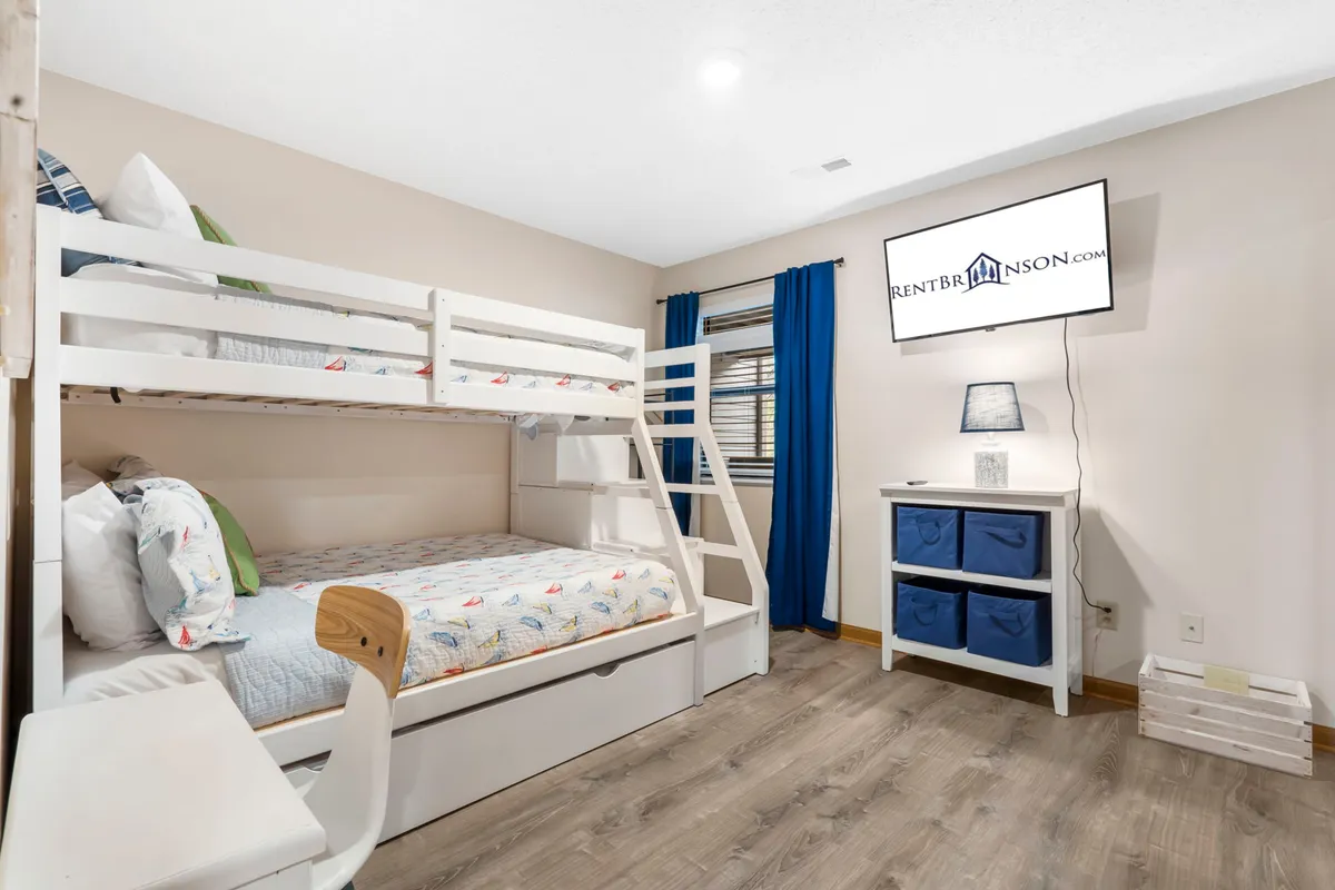 A playful, family-friendly bedroom with bunk beds (twin over full), a television, a desk with chair, and a decorative lamp. The space is cozy and functional, designed for both rest and entertainment, ideal for kids or multigenerational groups.