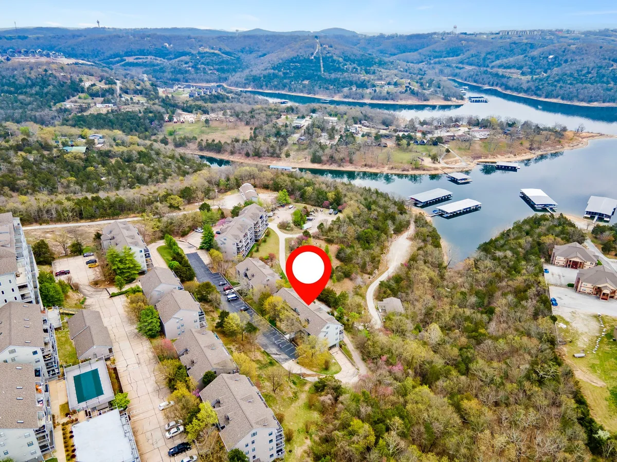 A scenic exterior view capturing the lake, rolling hills, residential buildings, and marina. The image suggests proximity to water activities like boating and fishing, with a peaceful natural environment and recreational opportunities.