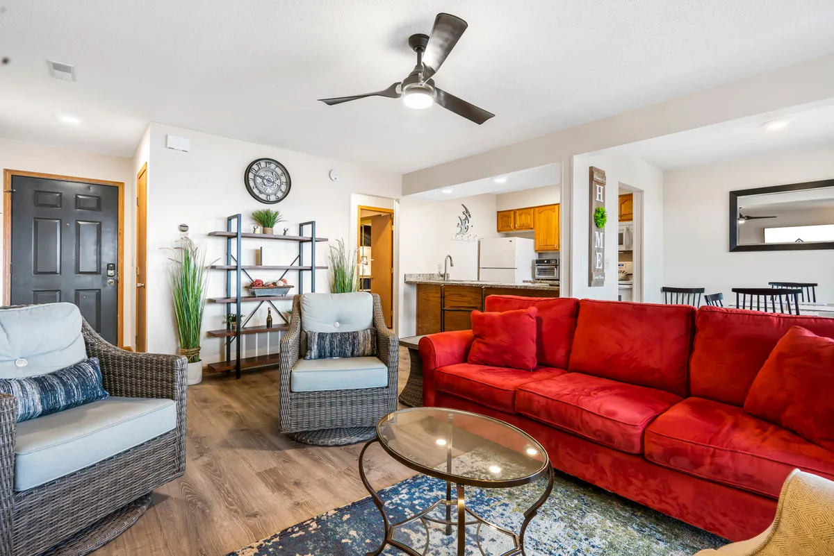 The image showcases a warm, inviting living area with a striking red sofa as the centerpiece, a decorative shelf adding a touch of homey charm, and a modern open kitchen perfect for shared meals. The cozy setup suggests a space ideal for relaxing movie nights, festive holiday gatherings, and memorable family time.