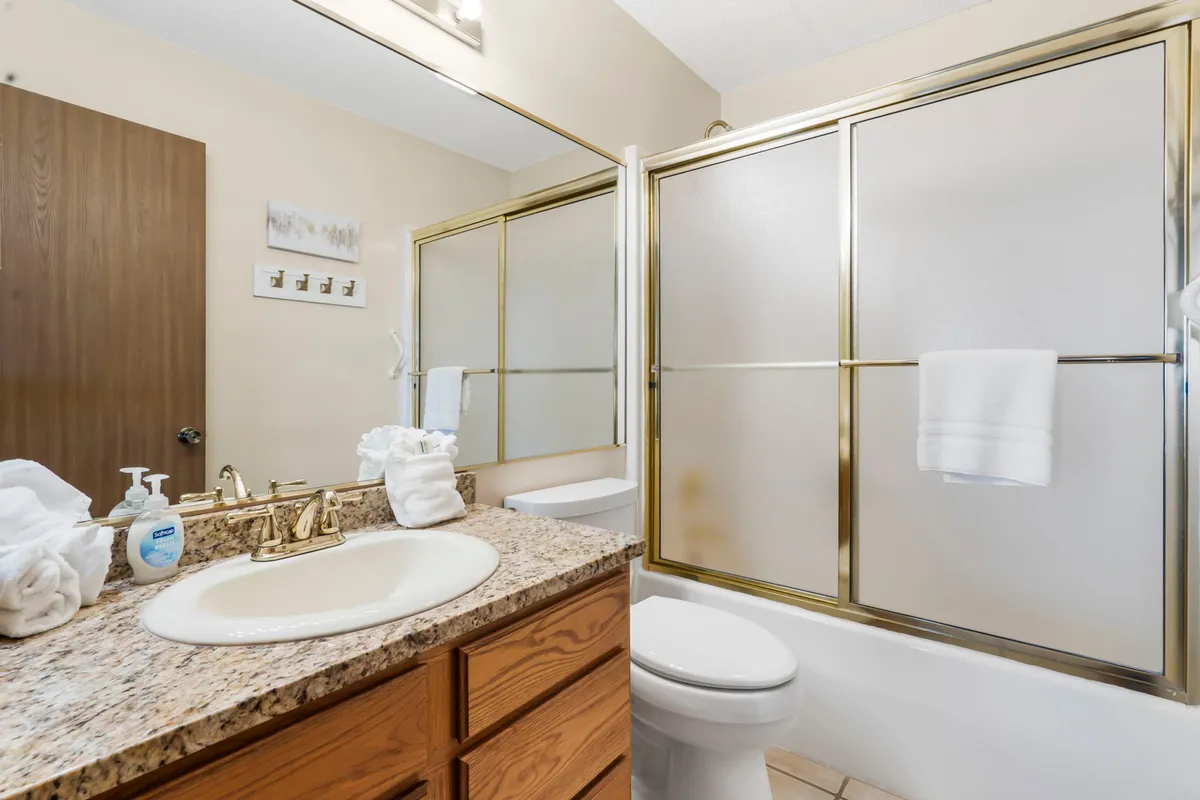 A spacious bathroom with a modern vanity and sink, large mirror, separate shower area, and toilet. The clean, refreshing design offers an inviting space for morning routines and evening relaxation.