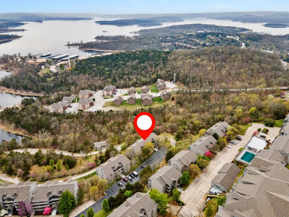 An elevated perspective encompassing the lush green landscape, residential buildings, the resort pool area, and the expanse of Table Rock Lake beyond. The inviting pool and the backdrop of water and greenery highlight a range of outdoor leisure possibilities.