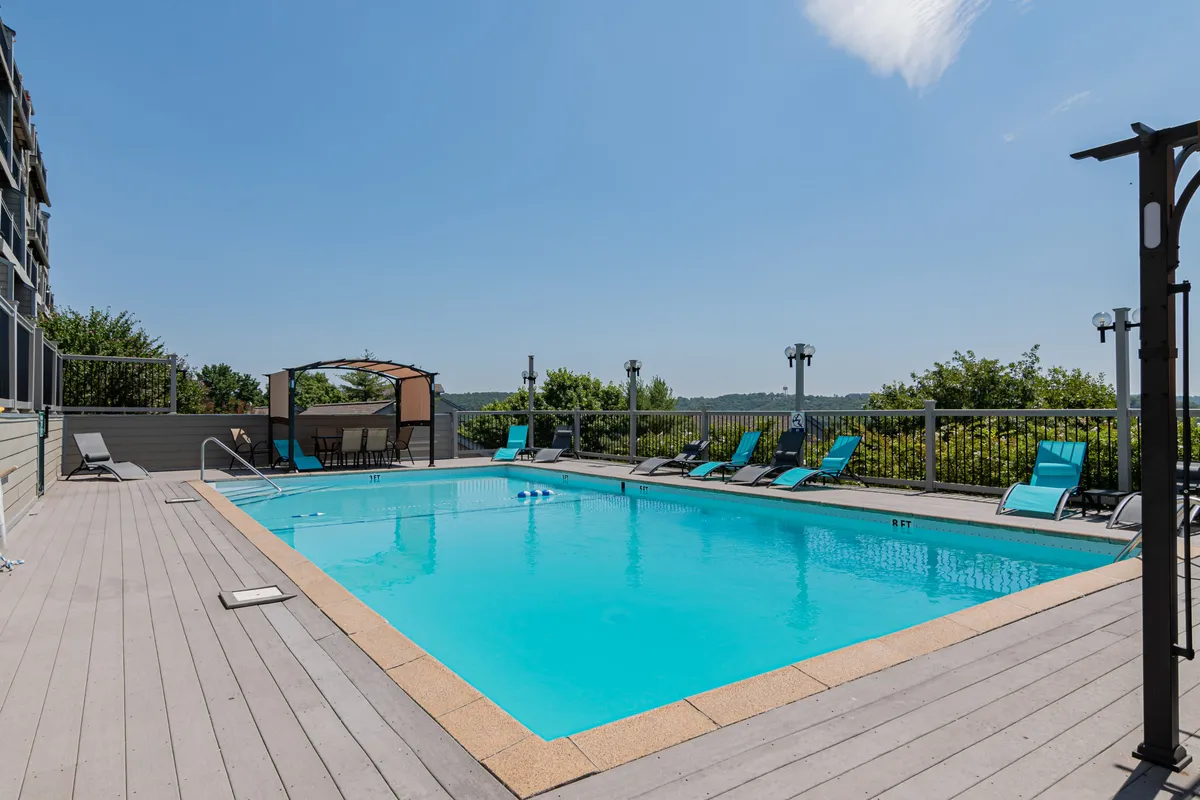 A tranquil resort pool featuring comfortable lounge chairs and a shaded canopy seating area. The pool is designed for both relaxation and socializing, surrounded by lush landscaping that adds a peaceful touch. The scene evokes leisurely afternoons, quiet mornings, and memorable summer pool parties.