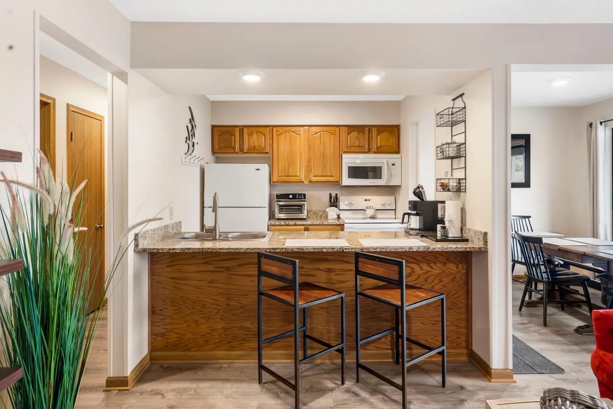 This image features a spacious kitchen island surrounded by bar stools and well-appointed cabinetry. The scene captures an open-concept layout, inviting both cooking and casual conversation. Ample counter space and visible modern appliances highlight functionality for meal preparation and entertaining.