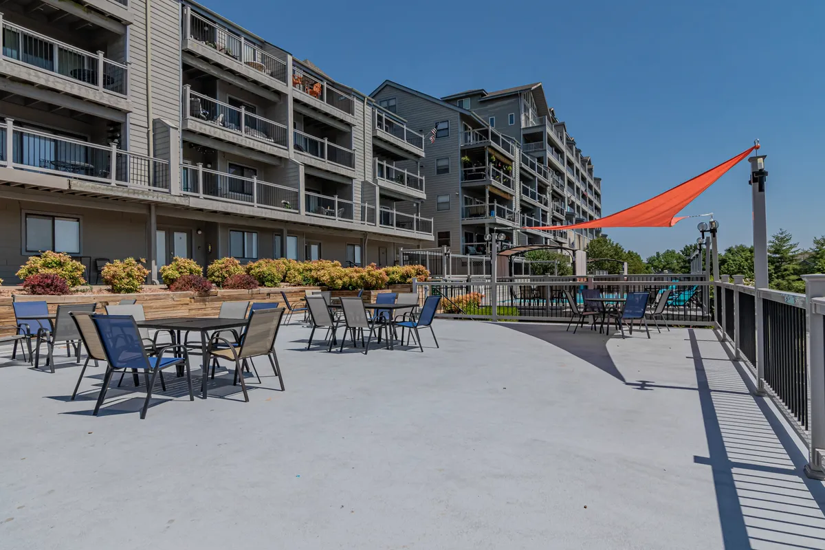 A cheerful outdoor seating area with colorful umbrellas, landscaped flower beds, and apartment balconies in the background. The space is set up for social gatherings, dining, or play, with a welcoming and lively atmosphere.