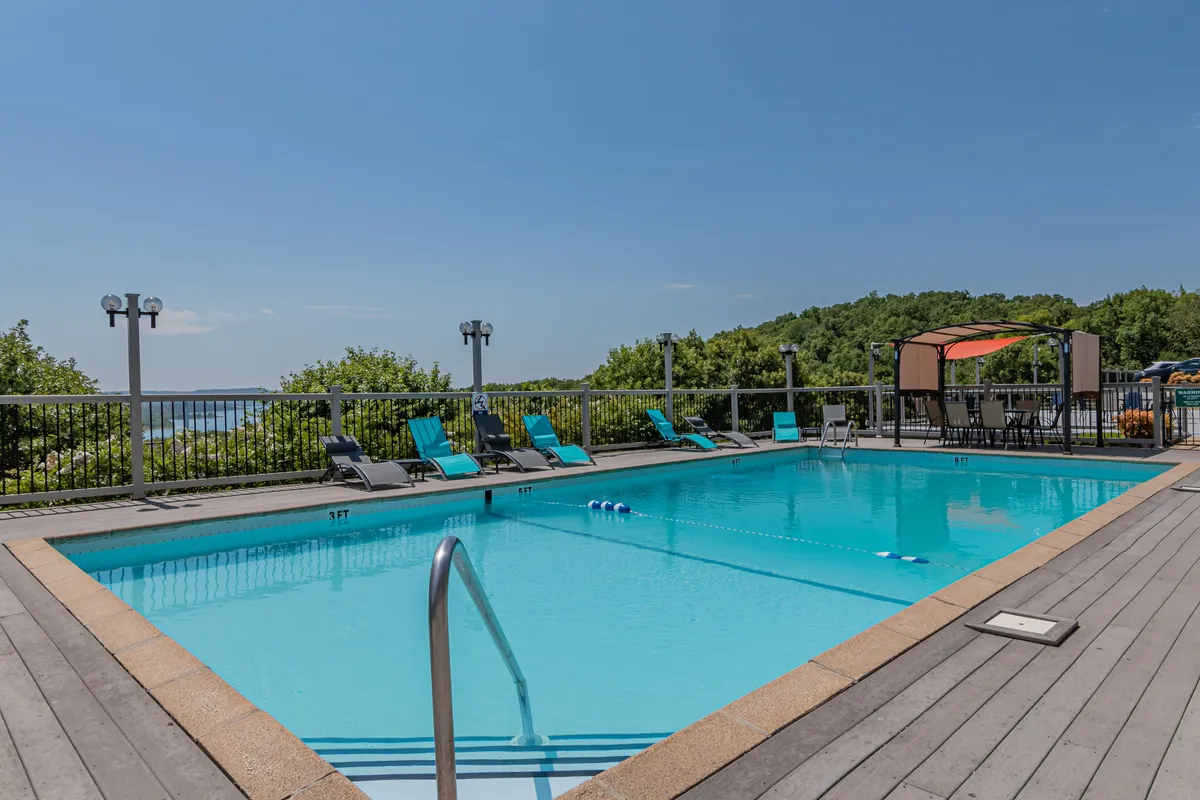 A vibrant outdoor swimming pool surrounded by inviting lounge chairs and set against a scenic landscape backdrop. The area is bathed in warm, natural light, creating the perfect spot for swimming, sunbathing, and socializing. The poolside atmosphere feels energetic yet relaxing, ideal for families and groups enjoying resort amenities in the warmer months.